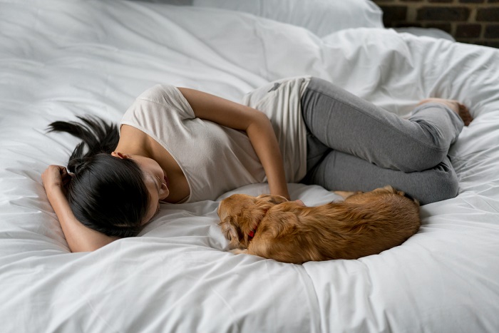 Woman relaxing at home lying on a bed stroking her dog.