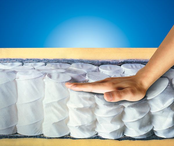 A hand pressing down on a cutaway of a pocketed coil mattress 