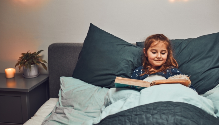 Little girl smiling as she reads a big book in bed