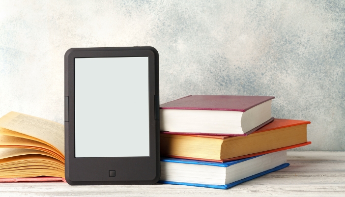 An e-reader sitting in front of a pile of physical books
