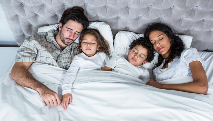 A family of four sleeps soundly together in a large bed.