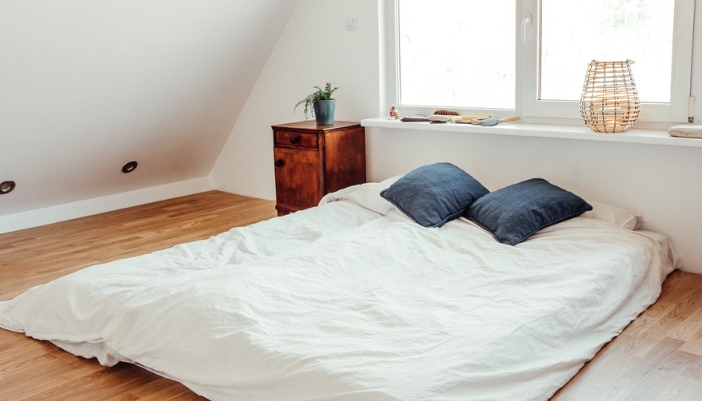 A thin mattress rests on the floor with minimal furniture around it.