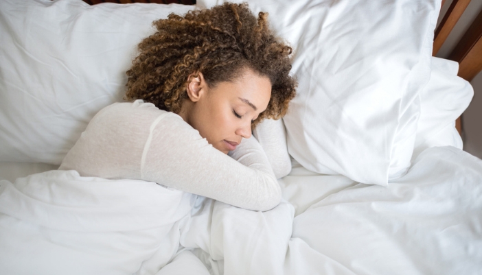 A young woman sleeps soundly on a white bed.