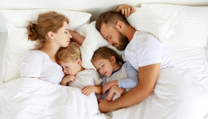 A man and woman sleep around two sleeping children in a white bed.
