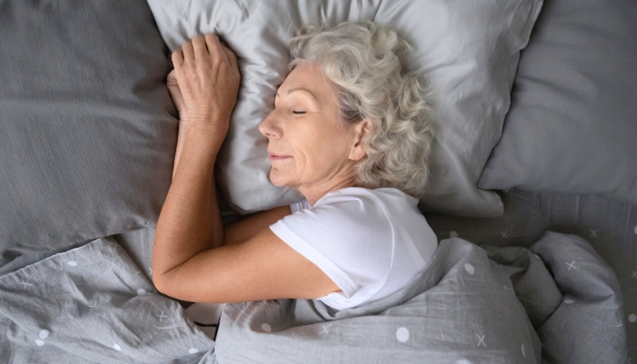 An elderly woman sleeps soundly in a gray bed.