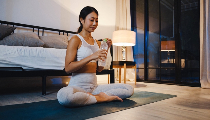 A woman sits in her bedroom and completes a nighttime yoga routine.