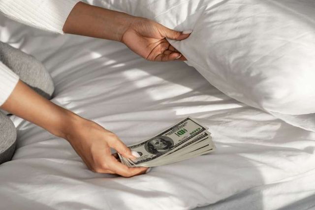 close view of a womans arms putting money under her pillow for a new mattress