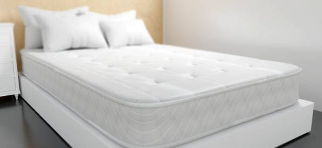 view of a white mattress on a white box spring with four pillows on top 