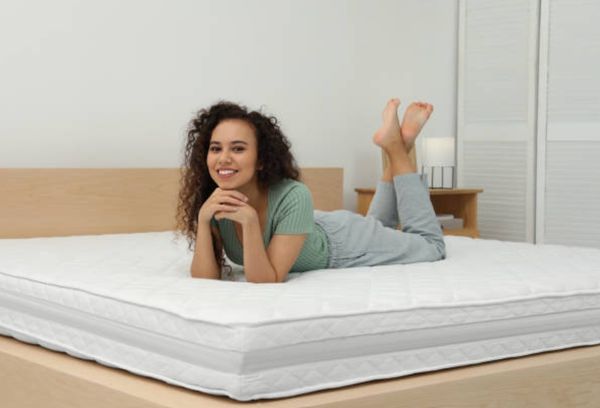 view of a woman laying on her stomach and smilining atop of a white mattress and beige box spring