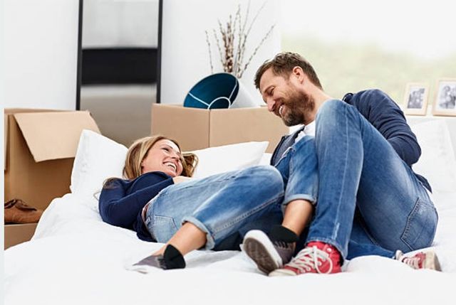 view of a couple sitting on their unboxed mattress a smiling