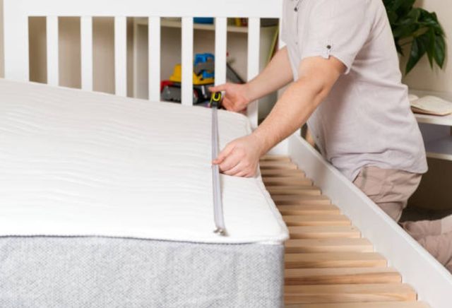 mattress-sizes view of a person measuring their mattress in a bedroom