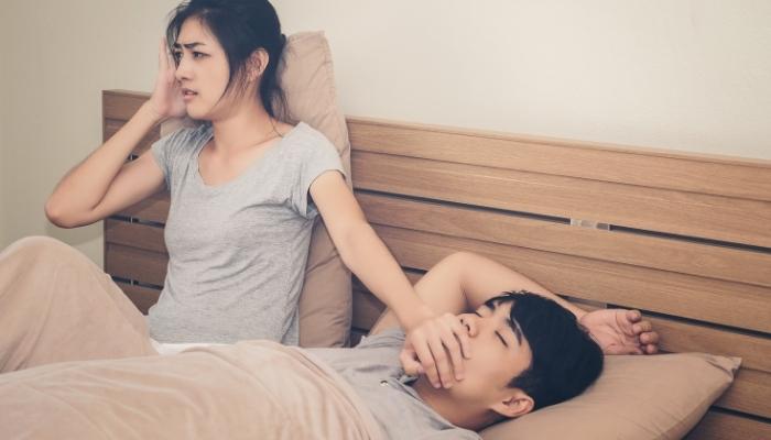 Woman holding pillow over her ear with one hand overing her partner’s mouth