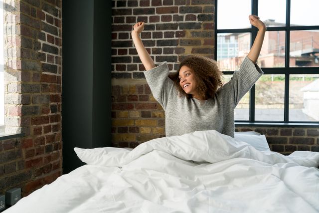 front view of a woman smiling and stretching after waking up in a rustic bedroom
