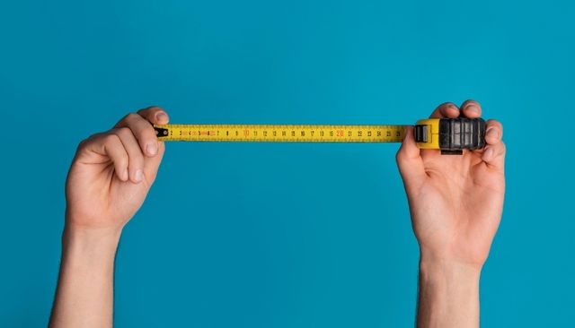 view of two hands holding a yellow measuring tape over a blue background