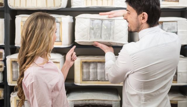 mattress-constructions view of a woman standing with a salesperson as he explains a mattress display showing various mattress types
