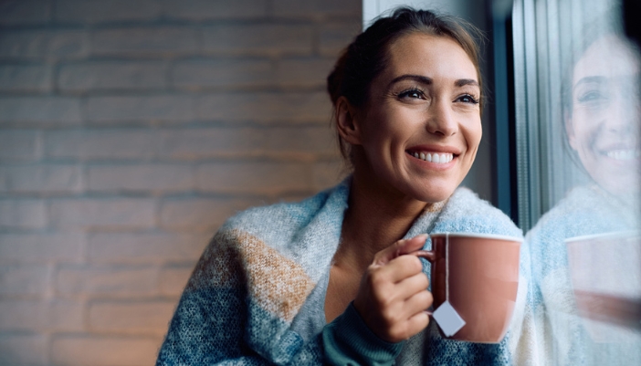 A woman happily drinks her cup of decaf tea.