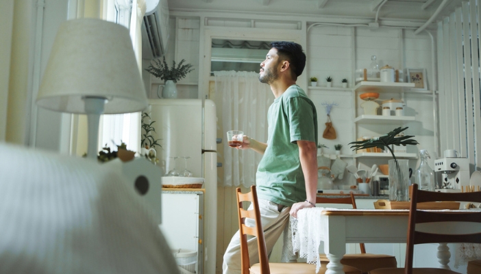 A man enjoys a cup of something in his well-lit kitchen. 