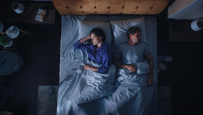 A man and woman lay in bed with their backs to each other.