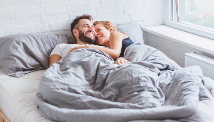 A man and woman laugh and cuddle in bed in the morning.