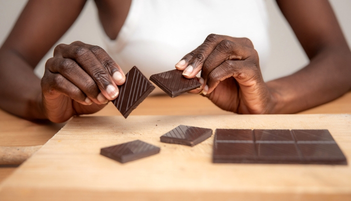 A pair of hands break apart pieces of a dark chocolate bar. 