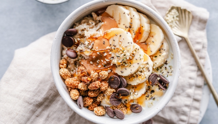 A close-up of a bowl of oatmeal with bananas, nuts, and chocolate on top.