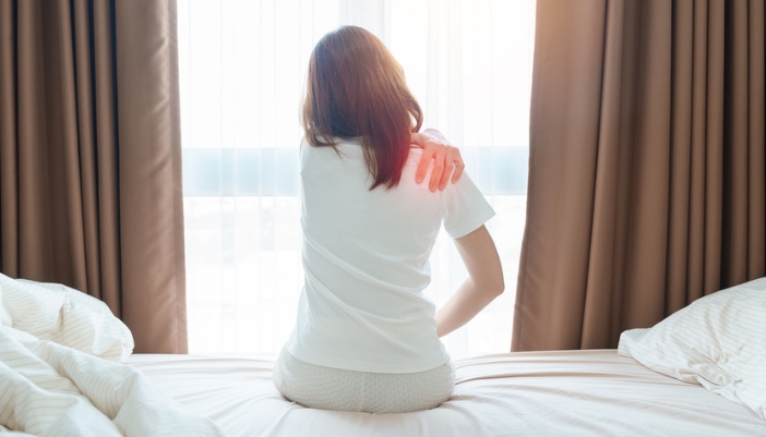 A woman rubs her shoulder after waking as if it pains her.