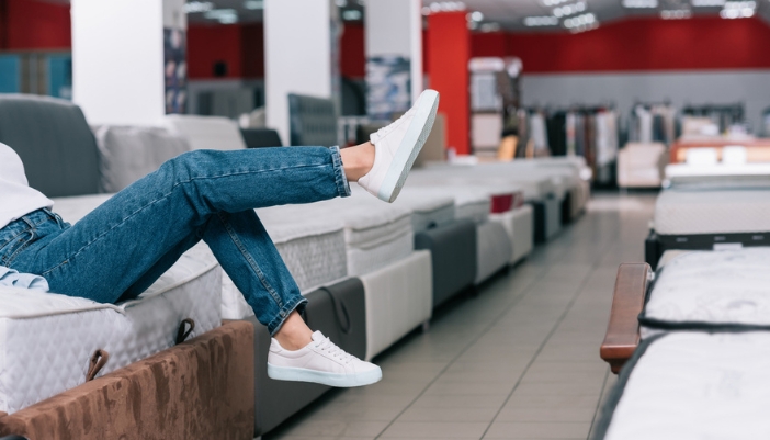 A woman shops for a mattress in a showroom and kicks her feet in the air. 