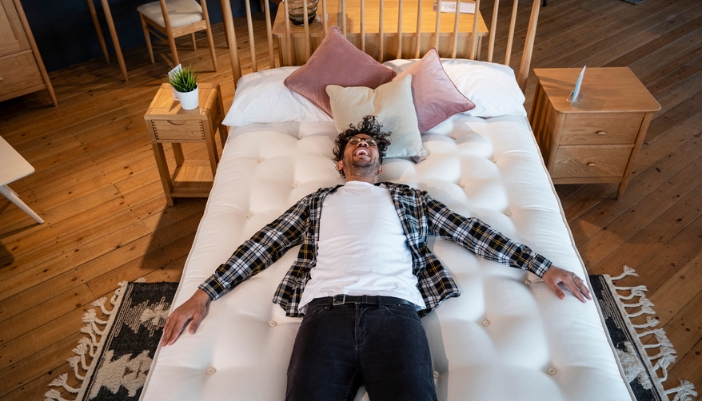 A man lays on a mattress in a showroom. 