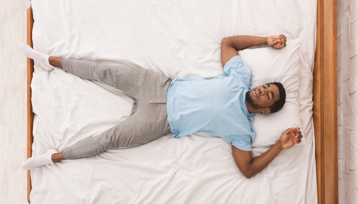 A man lays on his back across an entire queen bed.