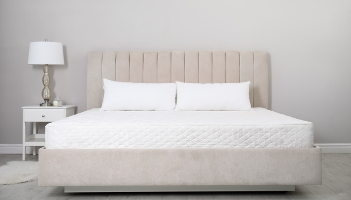A large mattress without sheets sits on an upholstered bed frame.