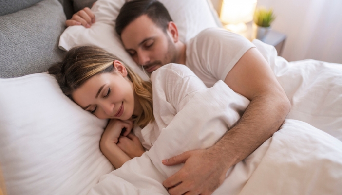 A couple sleeps curled together on their bed.