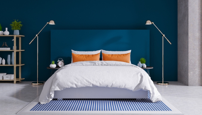 A white bed sits in front of a dark blue wall. 