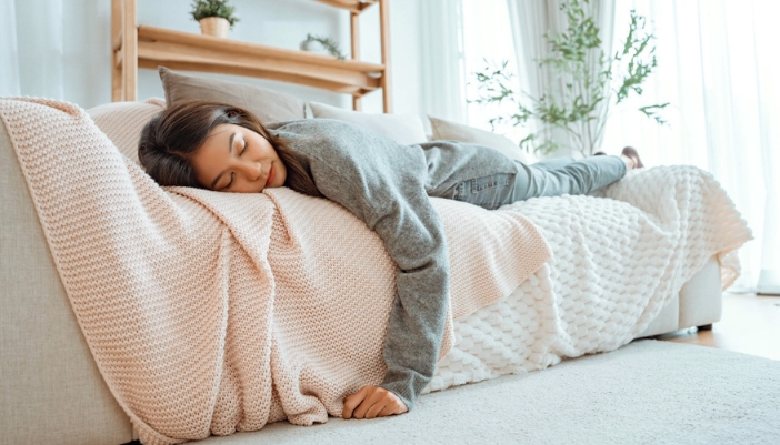 A woman sleeps on a white couch on a pink woven blanket.