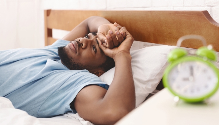 A tired man lays in bed and stares into space.