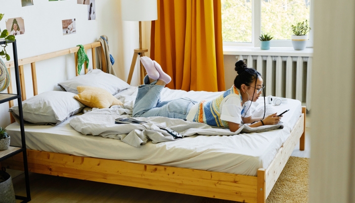 A teenage girl lays on her bed and uses her mobile phone at home.