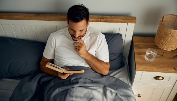 A man reads a book in bed at night.