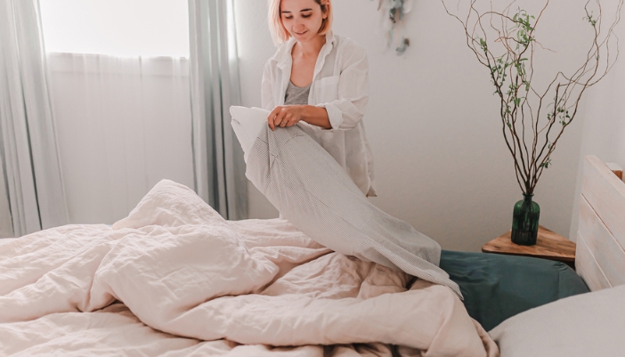 A woman makes her bed at home in the warm, morning light.
