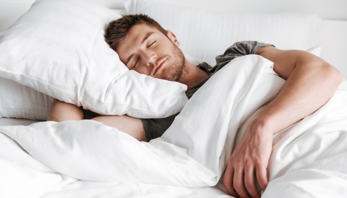 A man sleeps happily in his fluffy white comforter.