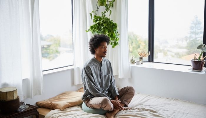 man sitting on his bed with his eyes closed and legs crossed