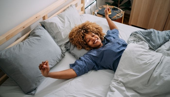 smiling woman in pajamas stretching arms in her bed at home