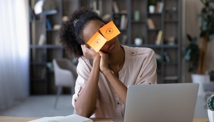Woman sleeping in front of laptop with sticky notes on her eyes