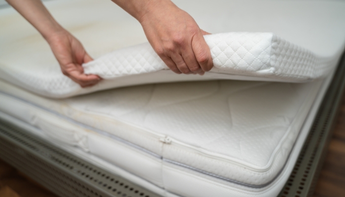 Closeup of hands placing thick mattress topper on the bed