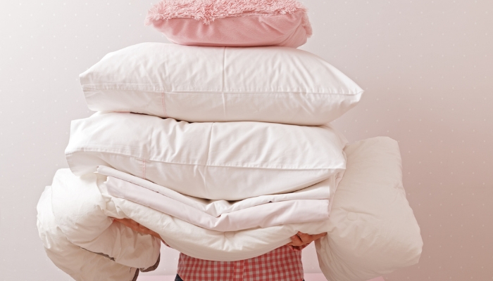 Woman holding a stack of pillows and bedding to wash
