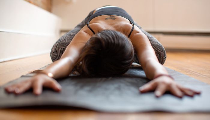 A woman on a yoga mat is leaning forward towards the camera in child’s pose