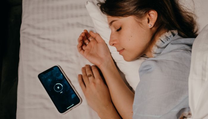 A woman naps on her bed with a timer next to her head