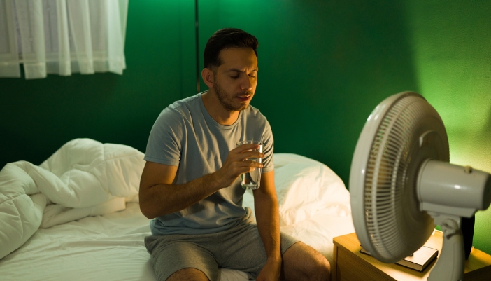 Man awake and drinking water in front of a fan