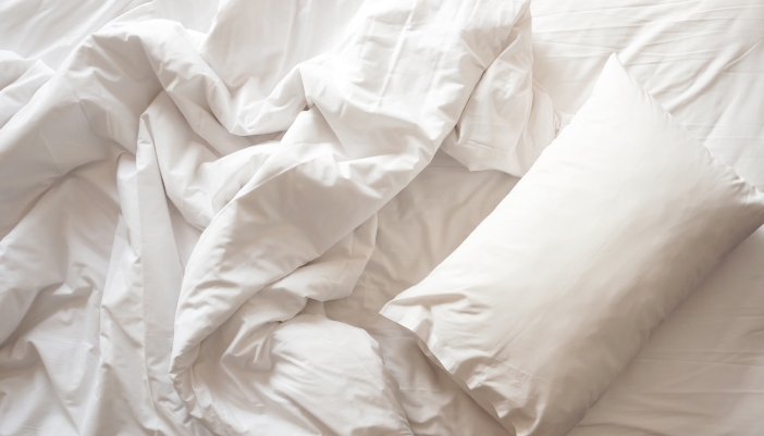 An overhead view of a mattress and pillow with linen sheets and covers