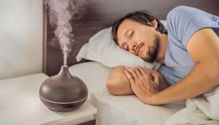A man sleeps soundly in bed with an essential oil diffuser on his nightstand.