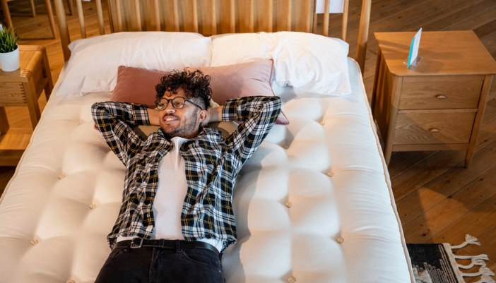 A young man lays on a mattress in a furniture store.