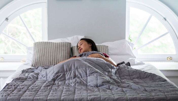 A woman sleeps happily under a gray weighted blanket.